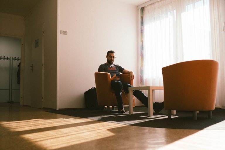 Prima ta sarcină de achiziții, pregătită în sala de așteptare Bărbat în casca de protecție, cu telefonul în mână, pe un scaun de așteptare